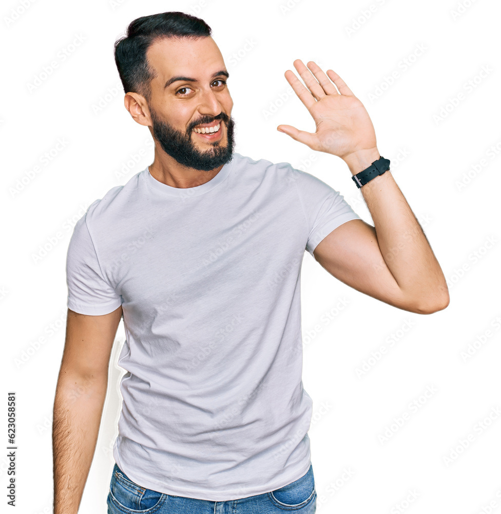 Young man with beard wearing casual white t shirt waiving saying hello happy and smiling, friendly welcome gesture Young man with beard wearing casual white t shirt waiving saying hello happy and smiling, friendly welcome gesture