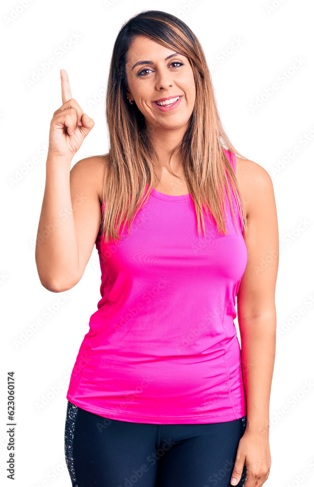 Young beautiful woman wearing sportswear showing and pointing up with finger number one while smiling confident and happy. Young beautiful woman wearing sportswear showing and pointing up with finger number one while smiling confident and happy.