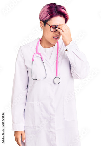 Young beautiful woman with pink hair wearing doctor uniform tired rubbing nose and eyes feeling fatigue and headache. stress and frustration concept.