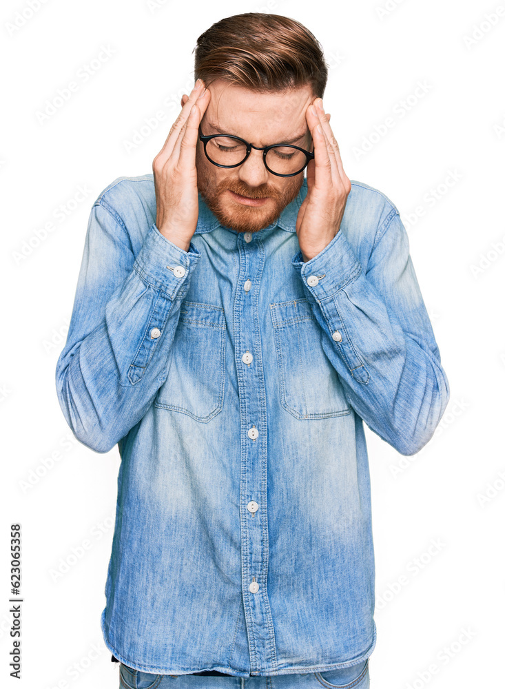 Young redhead man wearing casual denim shirt with hand on head for pain in head because stress. suffering migraine. Young redhead man wearing casual denim shirt with hand on head for pain in head because stress. suffering migraine.