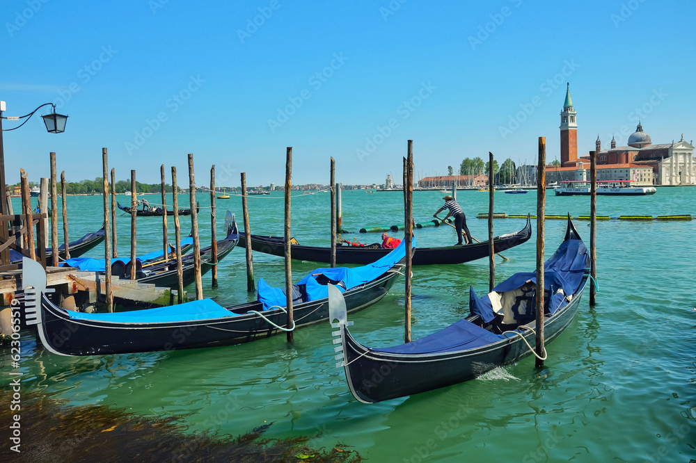 View from Riva degli Schiavoni on gondolas moored with palines, gondolas riding the Giudecca Canal and San Giorgio Maggiore in Venice, Italy.