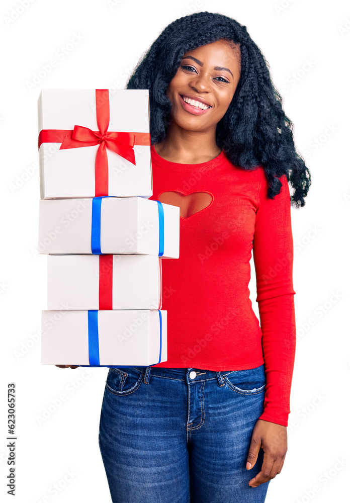 Beautiful african american woman holding presents looking positive and happy standing and smiling with a confident smile showing teeth Beautiful african american woman holding presents looking positive and happy standing and smiling with a confident smile showing teeth