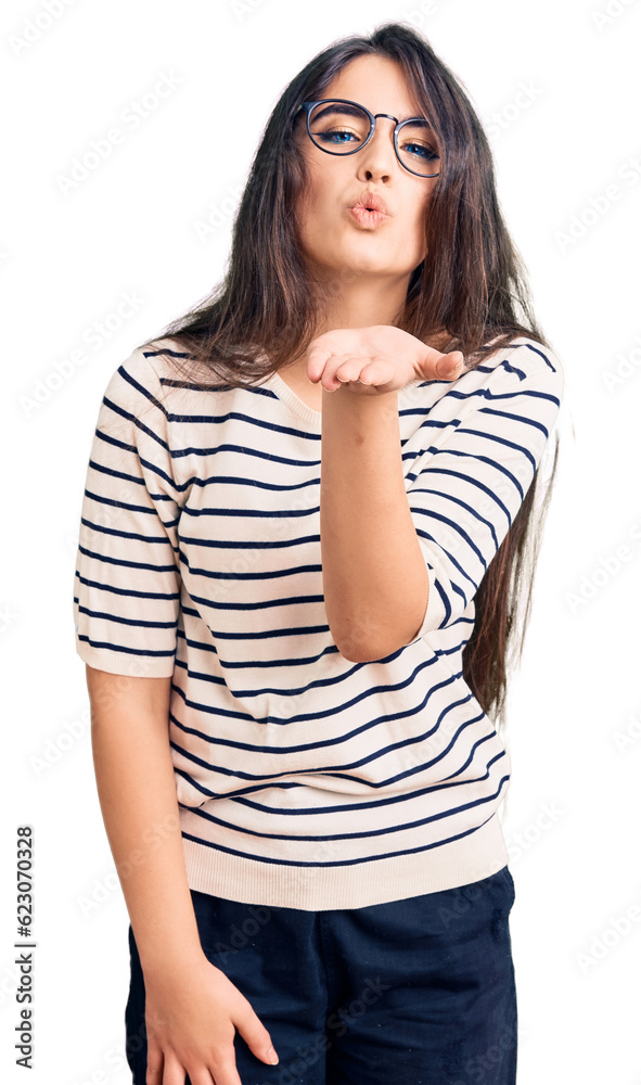 Brunette teenager girl wearing casual clothes and glasses looking at the camera blowing a kiss with hand on air being lovely and sexy. love expression. Brunette teenager girl wearing casual clothes and glasses looking at the camera blowing a kiss with hand on air being lovely and sexy. love expression.