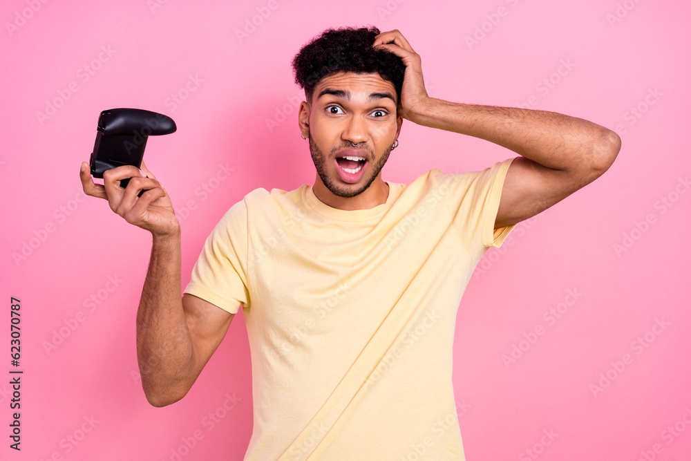 Portrait of astonished disappointed man dressed yellow t-shirt hold joystick arm on head lose game isolated on pink color background Portrait of astonished disappointed man dressed yellow t-shirt hold joystick arm on head lose game isolated on pink color background