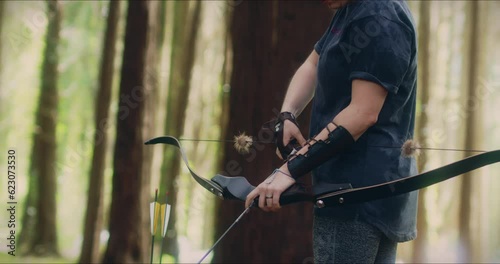 Archery girl loads her bow in a forest tilt medium shot photo