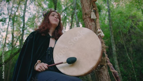 druid girl in a forest playing her shamanic drum low angle medium shot photo