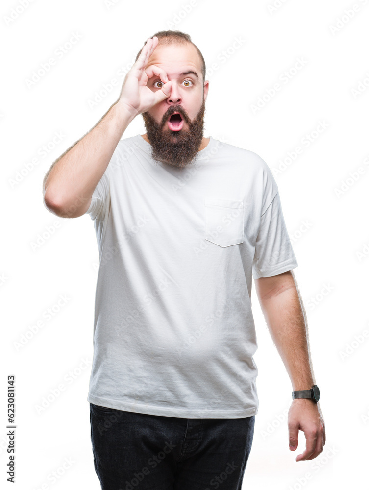 Young caucasian hipster man wearing casual t-shirt over isolated background doing ok gesture shocked with surprised face, eye looking through fingers. Unbelieving expression. Young caucasian hipster man wearing casual t-shirt over isolated background doing ok gesture shocked with surprised face, eye looking through fingers. Unbelieving expression.