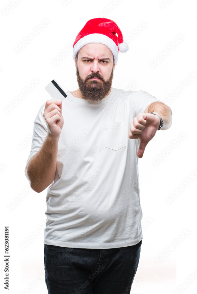 Young caucasian man wearing christmas hat holding credit card over isolated background with angry face, negative sign showing dislike with thumbs down, rejection concept Young caucasian man wearing christmas hat holding credit card over isolated background with angry face, negative sign showing dislike with thumbs down, rejection concept