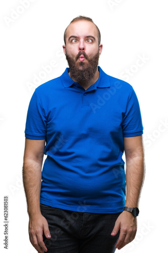 Young caucasian hipster man wearing blue shirt over isolated background making fish face with lips, crazy and comical gesture. Funny expression. © Krakenimages.com