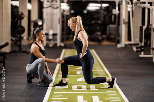 Obraz na plátně A happy female personal instructor is helping sportswoman with lunges in a gym