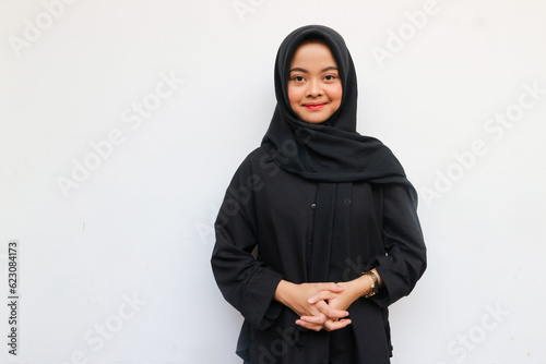 Beautiful young Asian woman in black shirt and hijab smiling happy and looking confident isolated over white background