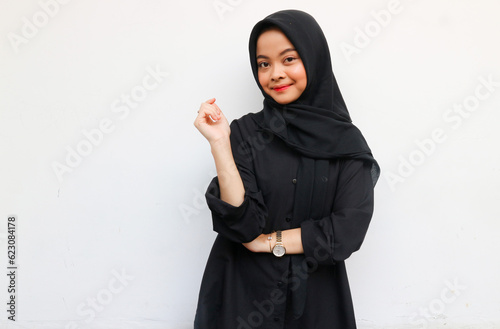 Beautiful young Asian woman in black shirt and hijab smiling happy and looking confident isolated over white background