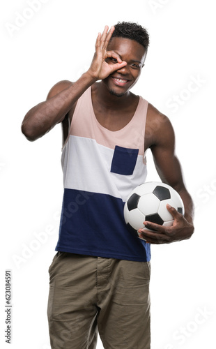 Young african american man holding soccer football ball with happy face smiling doing ok sign with hand on eye looking through fingers