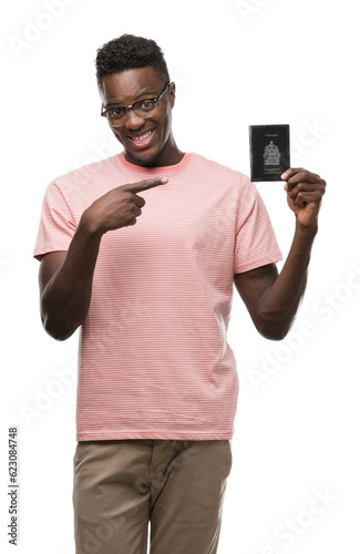 Young african american man holding canadian passport very happy pointing with hand and finger © Krakenimages.com