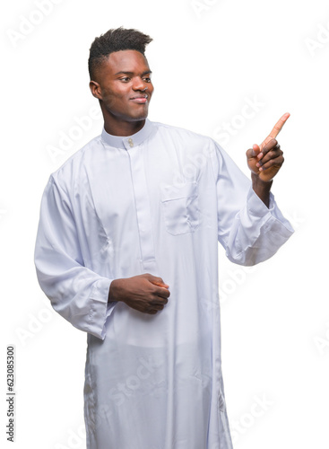 Young arabic african man wearing traditional djellaba over isolated background with a big smile on face, pointing with hand and finger to the side looking at the camera. photo