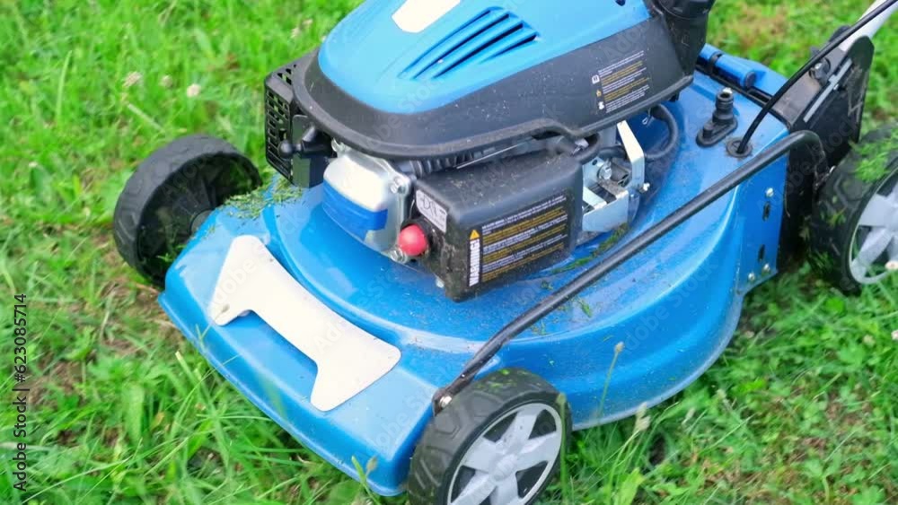 Lawn mower cutting grass. Small grass cuttings fly out of lawnmower. Grass clippings get spewed out of a mower pushed around by landscaper. Slow Motion. CloseUp. Gardener working with mower machine. Lawn mower cutting grass. Small grass cuttings fly out of lawnmower. Grass clippings get spewed out of a mower pushed around by landscaper. Slow Motion. CloseUp. Gardener working with mower machine.