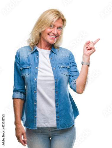 Middle age blonde woman over isolated background with a big smile on face, pointing with hand and finger to the side looking at the camera.