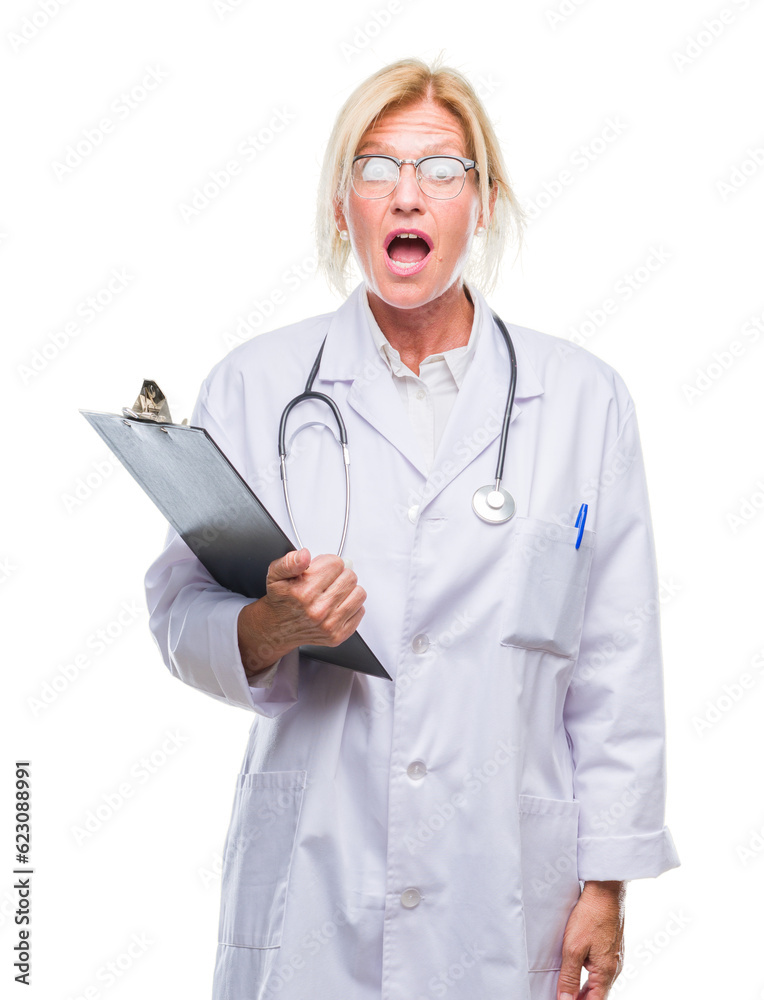 Middle age blonde doctor woman holding clipboard over isolated background scared in shock with a surprise face, afraid and excited with fear expression Middle age blonde doctor woman holding clipboard over isolated background scared in shock with a surprise face, afraid and excited with fear expression