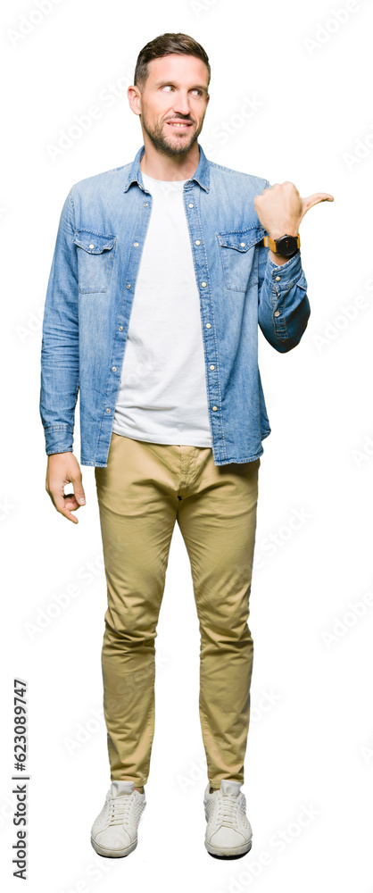 Handsome man with blue eyes and beard wearing denim jacket smiling with happy face looking and pointing to the side with thumb up.