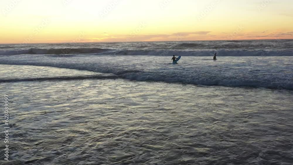 Two Surfer friends carving large breaking wave at colorful summer sunset. Surfer amateurs ride a board in the ocean at sunset Two Surfer friends carving large breaking wave at colorful summer sunset. Surfer amateurs ride a board in the ocean at sunset