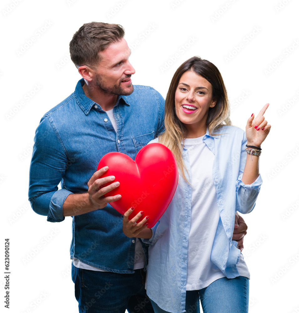 Young couple in love holding red heart over isolated background very happy pointing with hand and finger to the side Young couple in love holding red heart over isolated background very happy pointing with hand and finger to the side