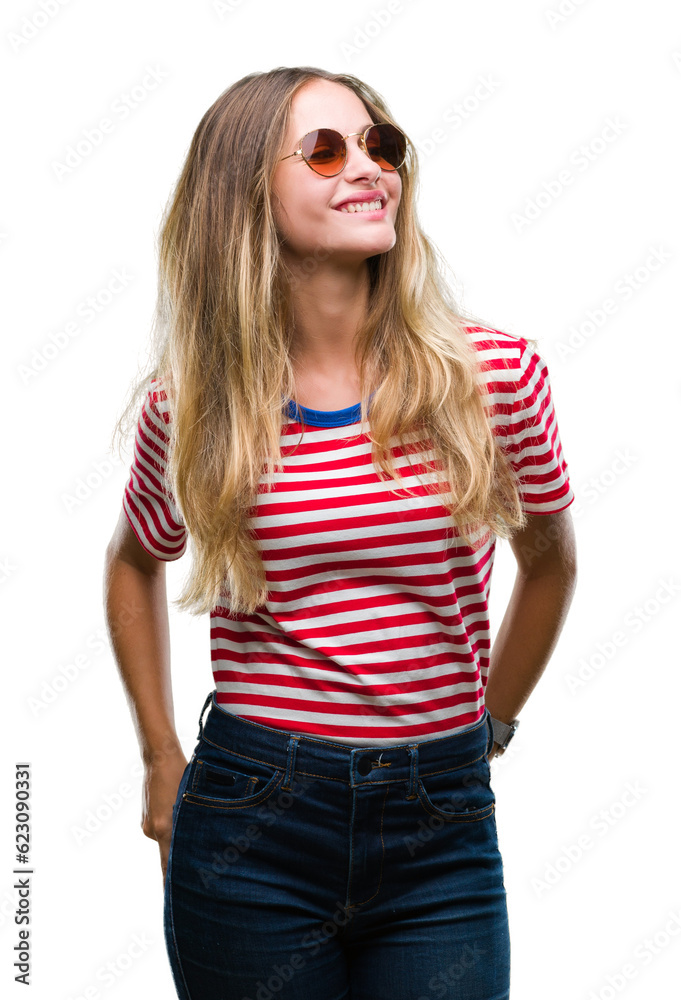 Young beautiful blonde woman wearing sunglasses over isolated background looking away to side with smile on face, natural expression. Laughing confident. Young beautiful blonde woman wearing sunglasses over isolated background looking away to side with smile on face, natural expression. Laughing confident.
