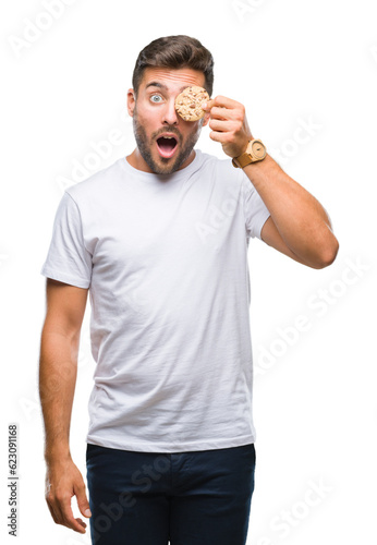 Young handsome man eating chocolate chips cookie over isolated background scared in shock with a surprise face, afraid and excited with fear expression