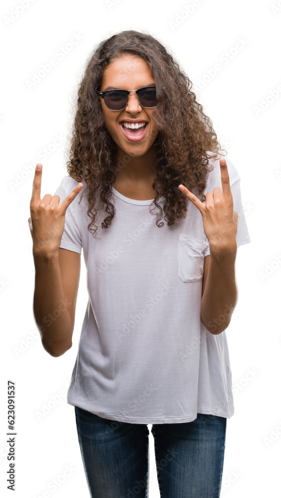 Young hispanic woman wearing sunglasses shouting with crazy expression doing rock symbol with hands up. Music star. Heavy concept.