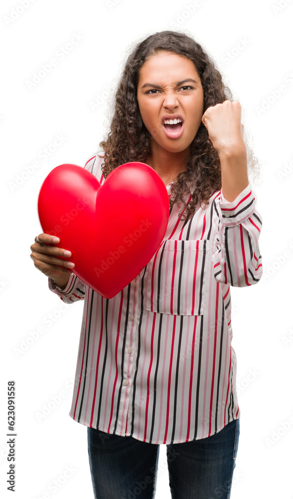Young hispanic woman in love holding red heart annoyed and frustrated shouting with anger, crazy and yelling with raised hand, anger concept Young hispanic woman in love holding red heart annoyed and frustrated shouting with anger, crazy and yelling with raised hand, anger concept