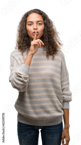 Beautiful young hispanic woman wearing stripes sweater asking to be quiet with finger on lips. Silence and secret concept.