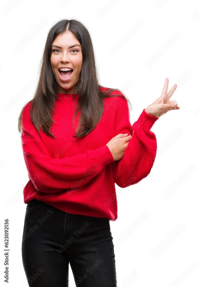 Young beautiful hispanic wearing red sweater smiling with happy face winking at the camera doing victory sign. Number two.