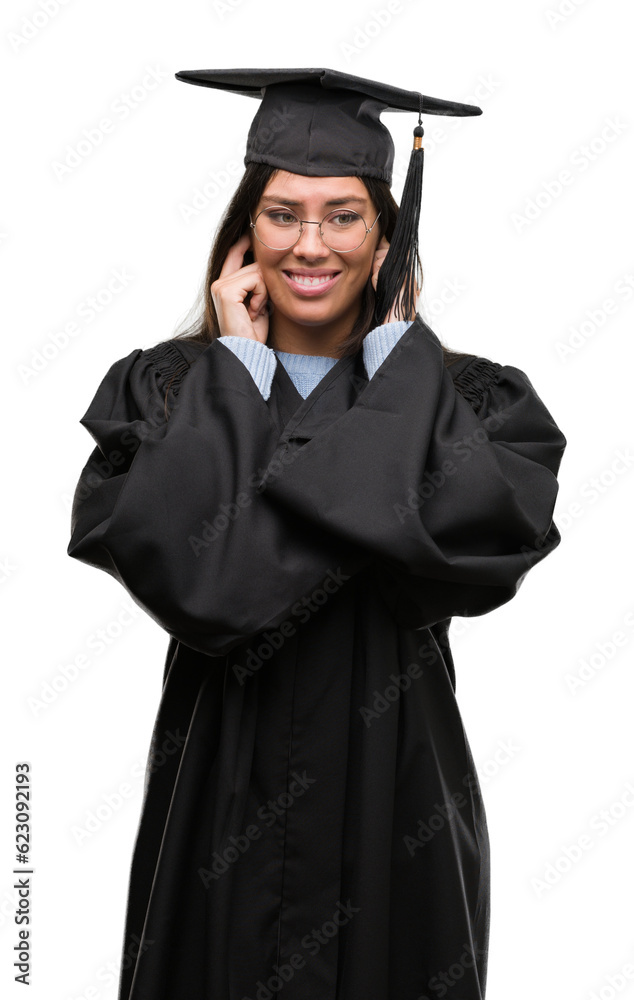 Young hispanic woman wearing graduated cap and uniform covering ears with fingers with annoyed expression for the noise of loud music. Deaf concept. Young hispanic woman wearing graduated cap and uniform covering ears with fingers with annoyed expression for the noise of loud music. Deaf concept.