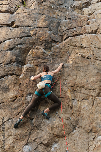 full-length back view of a young woman of athletic build rock climbing