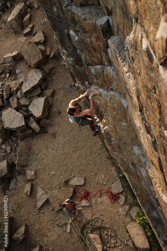 a young female athlete with big muscles on her arms, a pumped-up body climbing a cliff