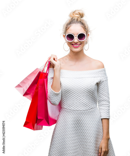 Young beautiful blonde woman holding shopping bags over isolated background with a happy face standing and smiling with a confident smile showing teeth