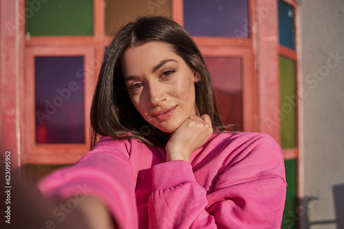 Lovely brunette girl making selfie at the summer street with vivid wall photo