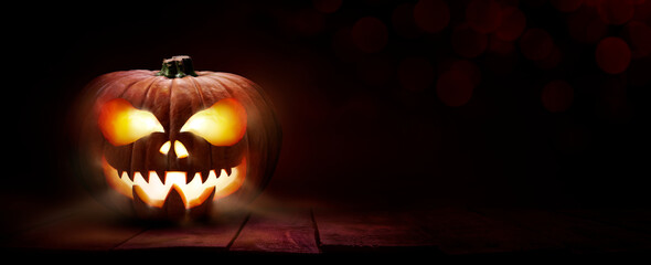 The spooky haunted evil glowing eyes of Jack O' Lanterns, halloween pumpkin, on the left of a wooden bench on a scary halloween night