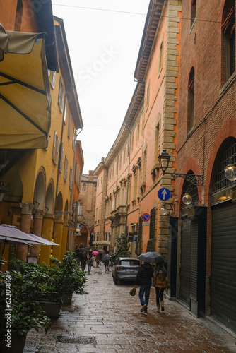 Bologna, Italy: Narrow streets of old town during rain. People sightseeing with umbrellas
