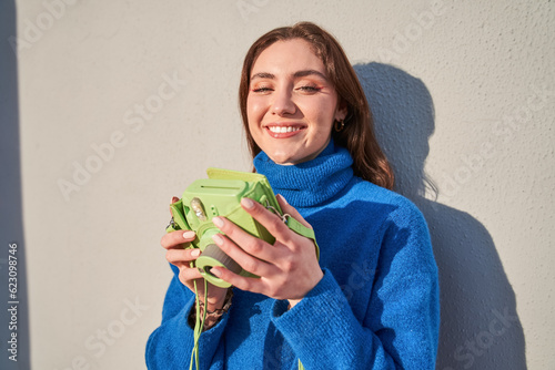 Happy teen woman holding green camera and posing with toothy smile photo