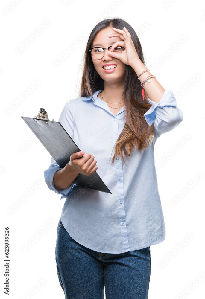 Young asian business woman holding clipboard over isolated background with happy face smiling doing ok sign with hand on eye looking through fingers Young asian business woman holding clipboard over isolated background with happy face smiling doing ok sign with hand on eye looking through fingers