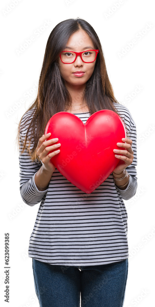 Young asian woman in love holding read heart over isolated background with a confident expression on smart face thinking serious Young asian woman in love holding read heart over isolated background with a confident expression on smart face thinking serious