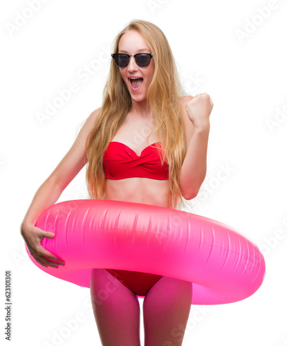 Valokuva Blonde teenager woman wearing bikini and holding pink floater screaming proud an