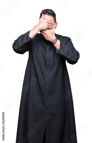 Young Christian priest over isolated background Covering eyes and mouth with hands, surprised and shocked. Hiding emotion