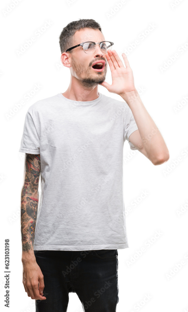 Young tattooed adult man shouting and screaming loud to side with hand on mouth. Communication concept. Young tattooed adult man shouting and screaming loud to side with hand on mouth. Communication concept.