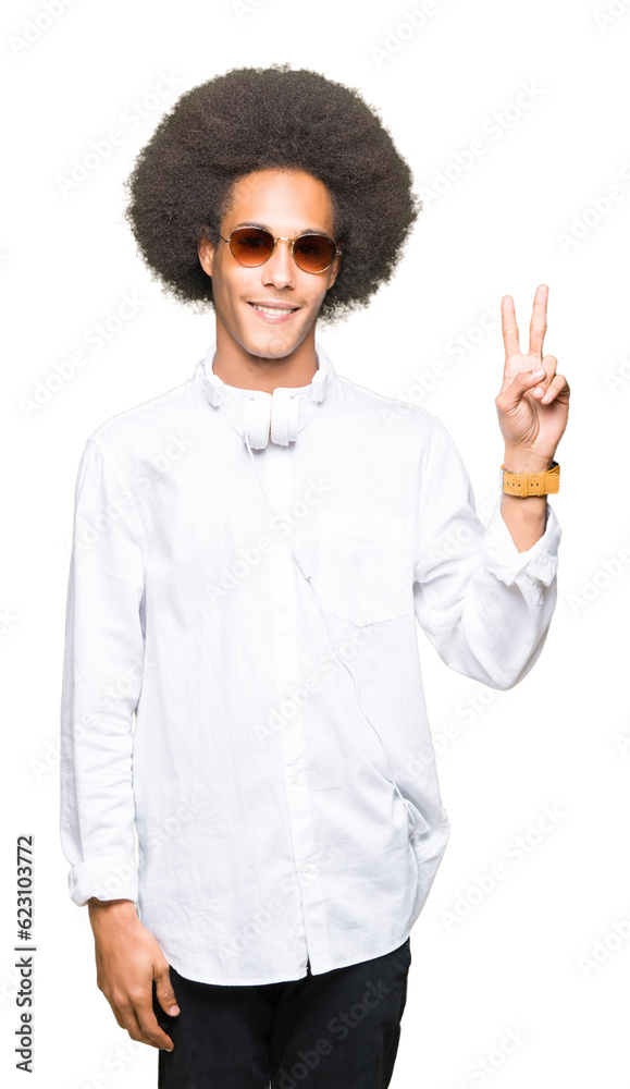 Young african american man with afro hair wearing sunglasses and headphones smiling with happy face winking at the camera doing victory sign. Number two. Young african american man with afro hair wearing sunglasses and headphones smiling with happy face winking at the camera doing victory sign. Number two.