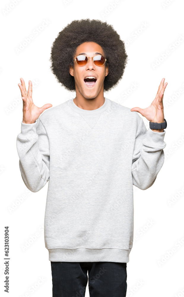 Young african american man with afro hair wearing sunglasses celebrating crazy and amazed for success with arms raised and open eyes screaming excited. Winner concept Young african american man with afro hair wearing sunglasses celebrating crazy and amazed for success with arms raised and open eyes screaming excited. Winner concept