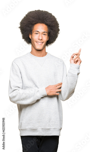 Young african american man with afro hair wearing sporty sweatshirt with a big smile on face, pointing with hand and finger to the side looking at the camera.