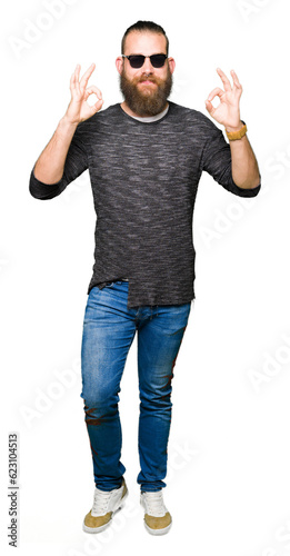 Young hipster man wearing sunglasses relax and smiling with eyes closed doing meditation gesture with fingers. Yoga concept. © Krakenimages.com
