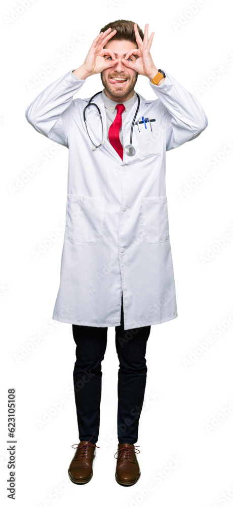 Young handsome doctor man wearing medical coat doing ok gesture like binoculars sticking tongue out, eyes looking through fingers. Crazy expression. Young handsome doctor man wearing medical coat doing ok gesture like binoculars sticking tongue out, eyes looking through fingers. Crazy expression.