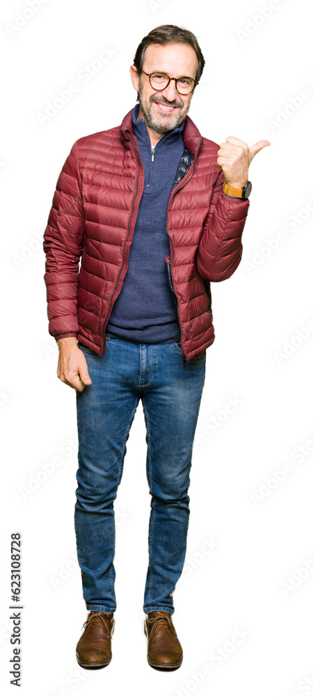Middle age handsome man wearing glasses and winter coat smiling with happy face looking and pointing to the side with thumb up. Middle age handsome man wearing glasses and winter coat smiling with happy face looking and pointing to the side with thumb up.